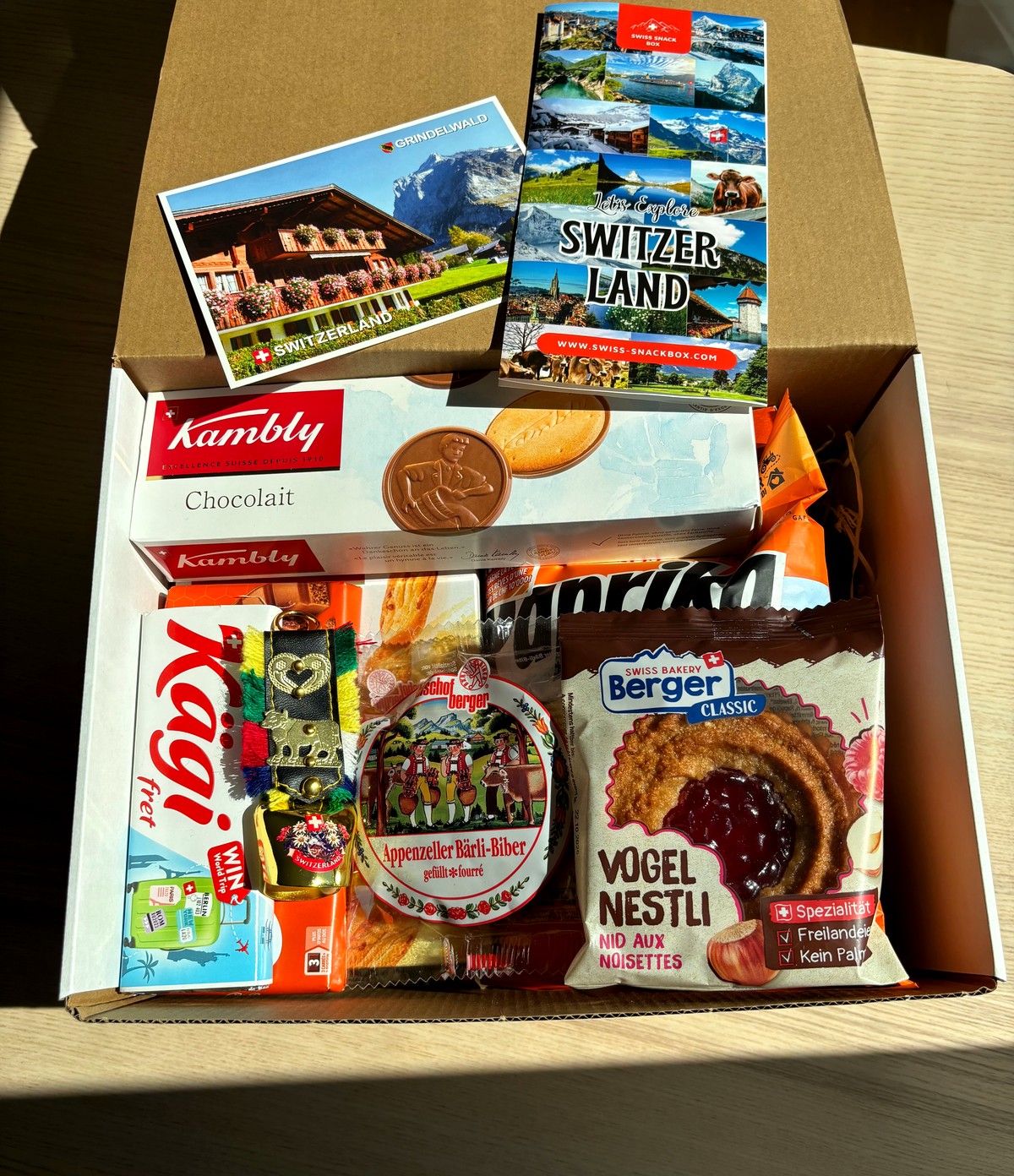 Swiss Snack Box opened, filled with Swiss snacks, a postcard and a food guide